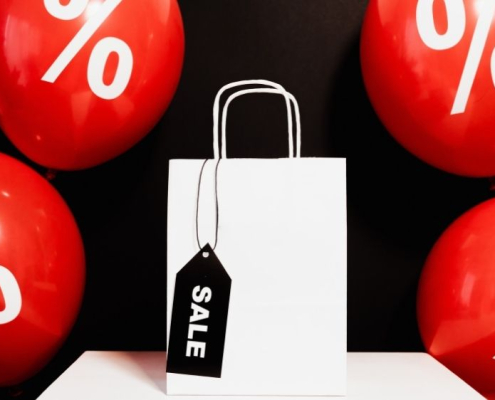 Ausgezeichnet.org spricht darüber, wie Händler sich auf das Angebotswochenende rund um "Black Friday" und Cyber Monday vorbereiten können, auf dem Bild sind eine Shoppingtüte und Ballons zu sehen mit der Aufschrift Sale