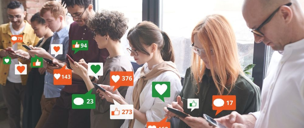 Ausgezeichnet.org erklärt virales Marketing und zeigt auf, wie es dazu kommen kann, das Bild zeigt eine Gruppe von Menschen am Smartphone, aus denen zur Verbildlichung Sprechblasen mit Likes und Kommentare aufsteigen