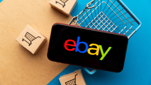 Handy mit ebay-Logo auf Einkaufskorb mit Ware | AUSGEZEICHNET.ORG